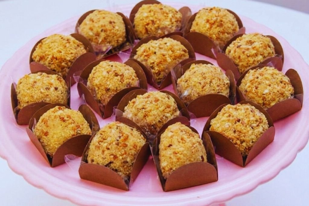 Como fazer brigadeiro de paçoca gourmet para vender. Apresentação profissional de docinhos cremosos passados na paçoca esfarelada sobre um prato rosa. Dica de doce altamente lucrativo para lucrar o ano inteiro.