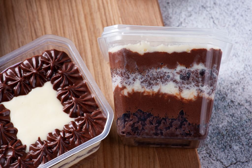 Foto de frente de um bolo de pote sabor Prestígio, destacando a montagem das camadas perfeitas através da embalagem transparente.